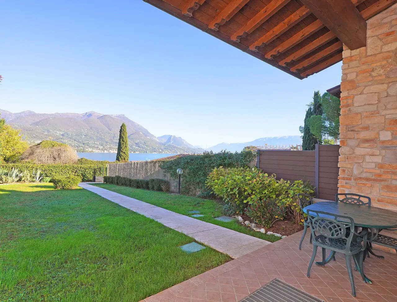 Giardino con prato, vialetto e tavolo con sedie sotto portico