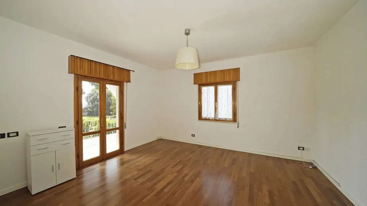 Soggiorno vuoto con pavimento in legno e due finestre con tende