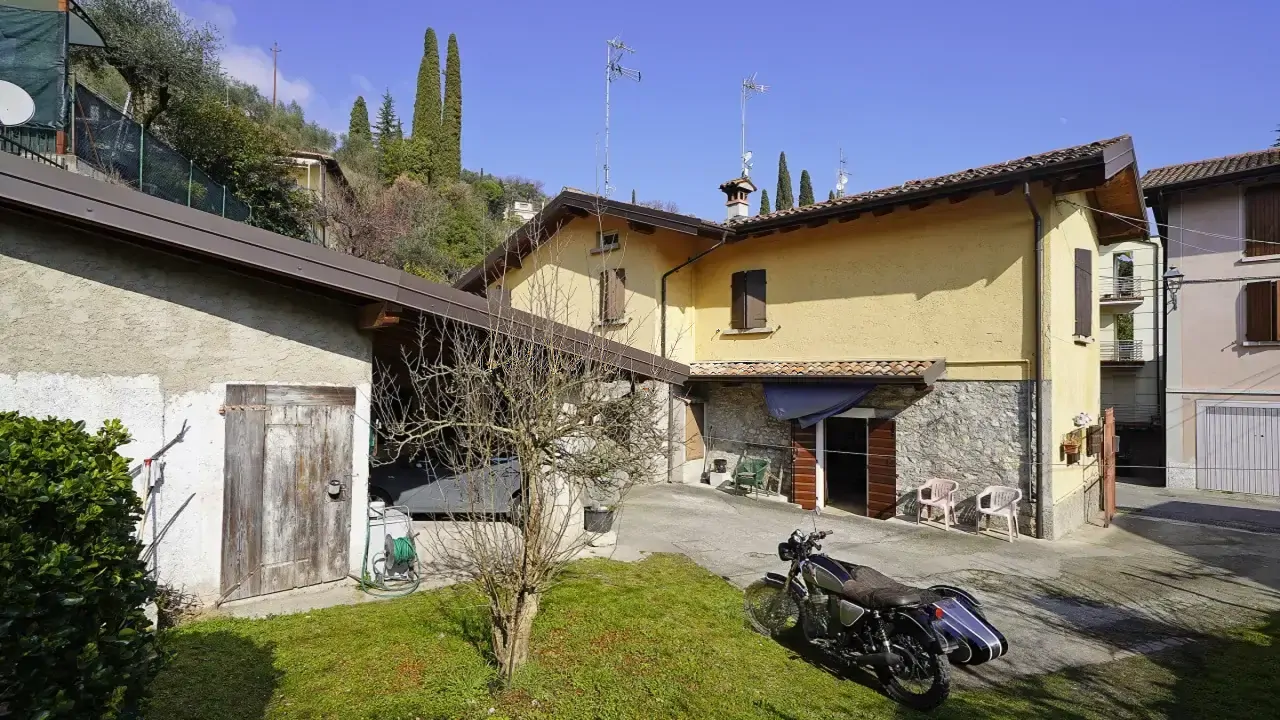 Corte privata con moto e albero davanti a casa gialla con tetto in tegole