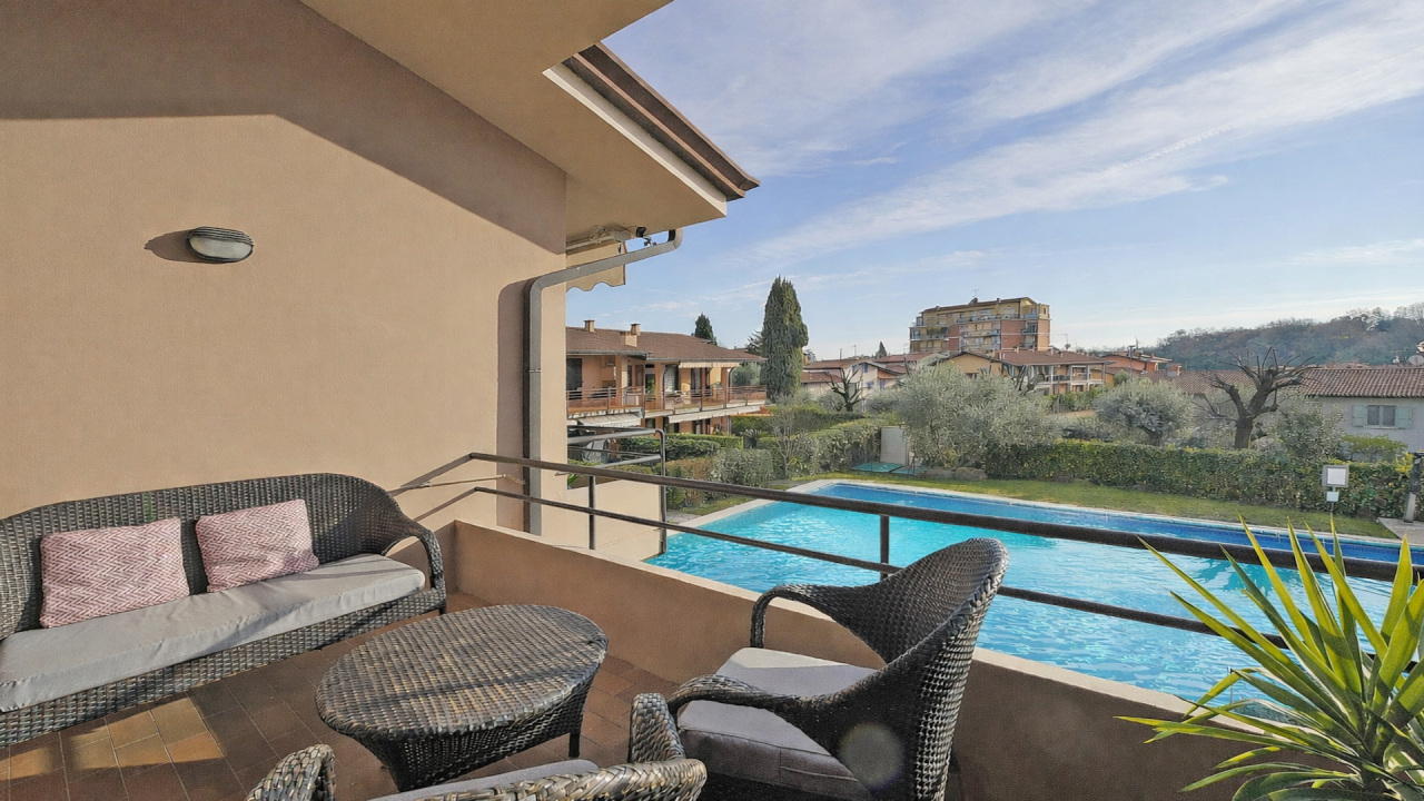 Terrasse mit Gartenmöbeln und Blick auf den Pool der Wohnanlage