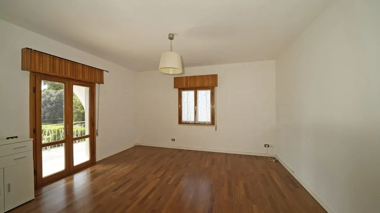 Soggiorno vuoto con pavimento in legno e due finestre con persiane in legno