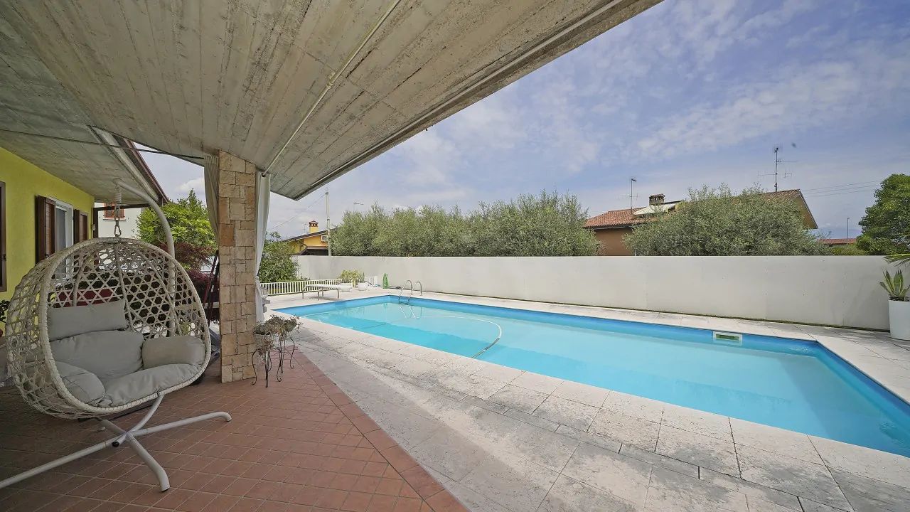 Piscina rettangolare con bordo in pietra e zona coperta con dondolo bianco
