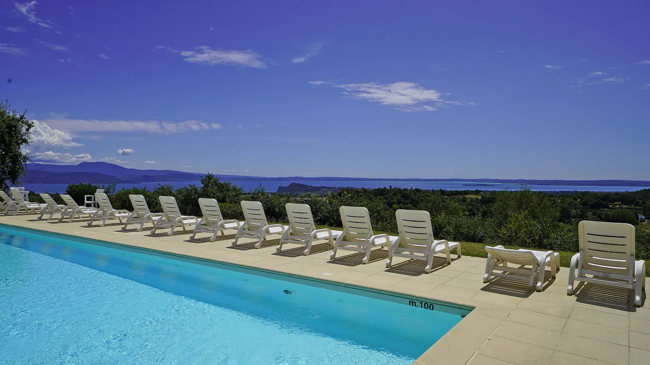 Swimming pool with sun loungers and view of lake and hills