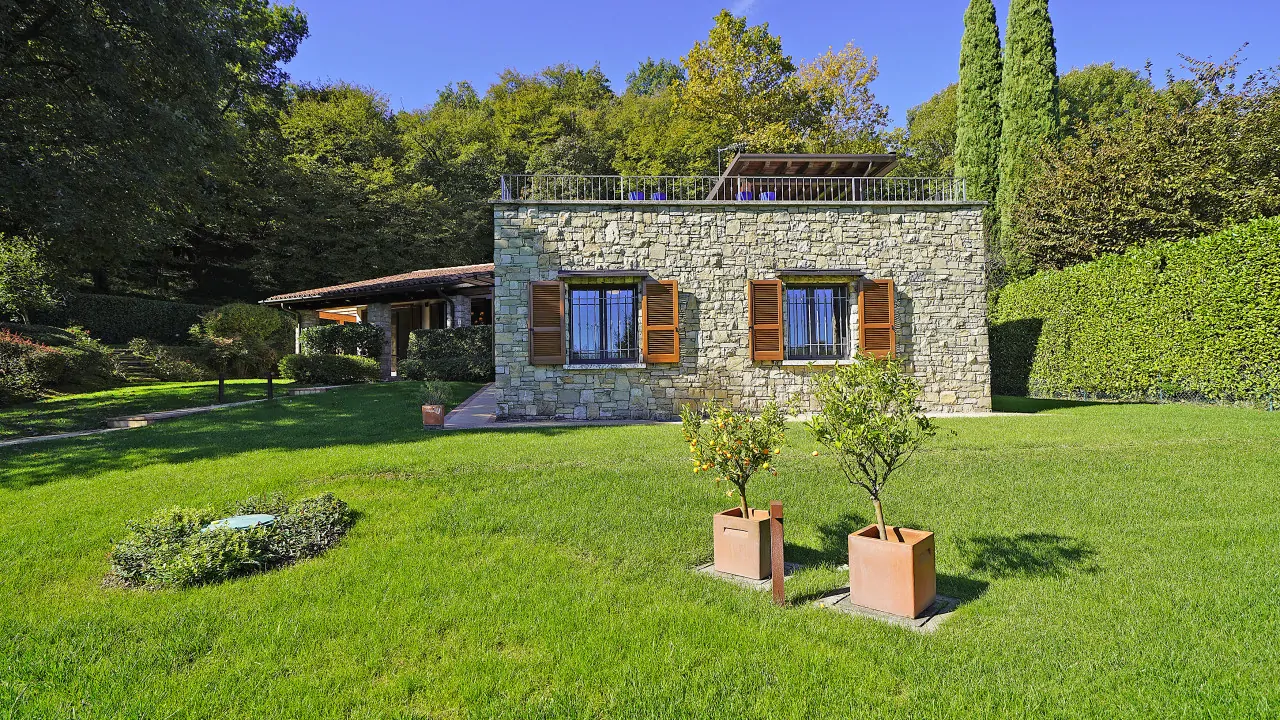 Giardino con prato verde e alberi in vaso davanti a villa in pietra