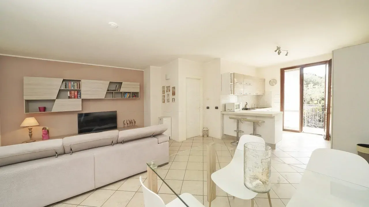 Wohnzimmer mit Sofa, TV-Möbel und offener Küche mit Glastür
