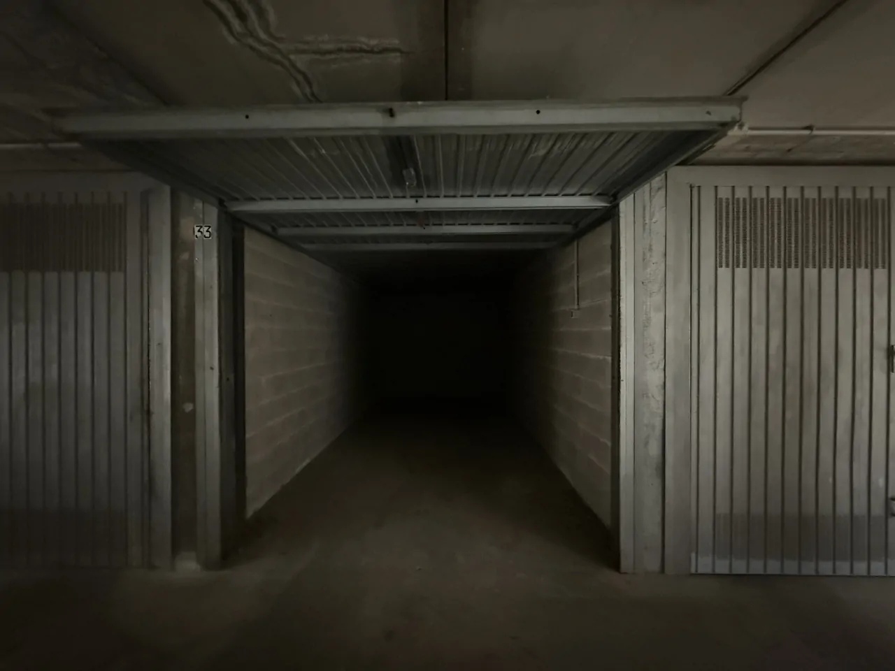 Garage con porta basculante aperta e pareti in cemento