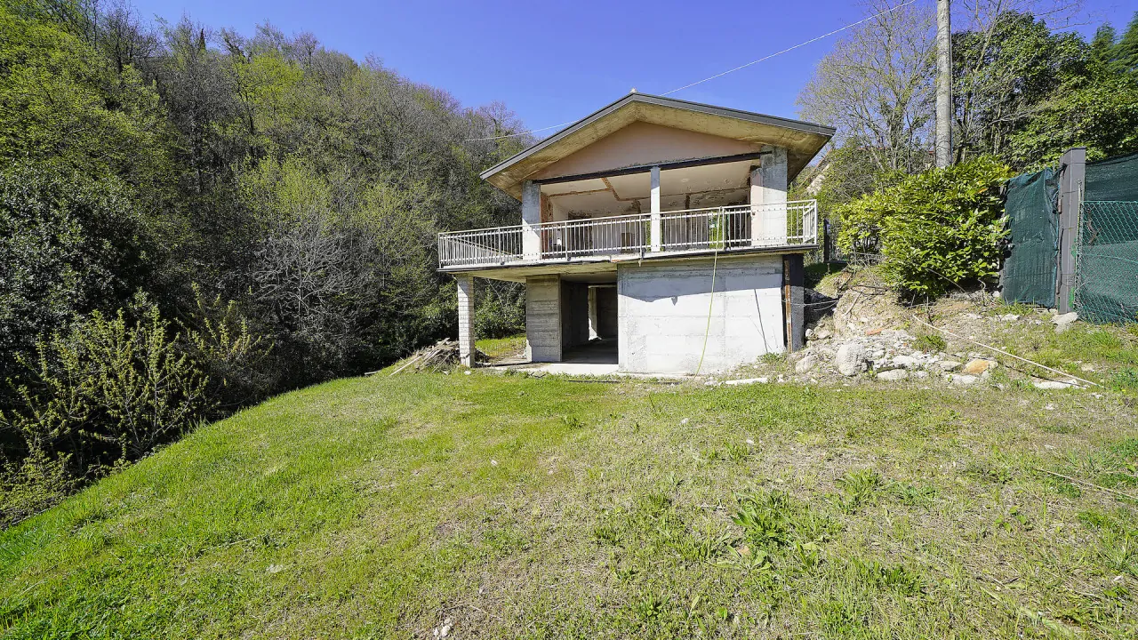 Rohbau-Villa mit Grasfläche und Bäumen im Hintergrund
