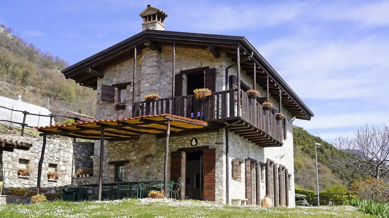 Stone farmhouse with balcony and pergola on green lawn