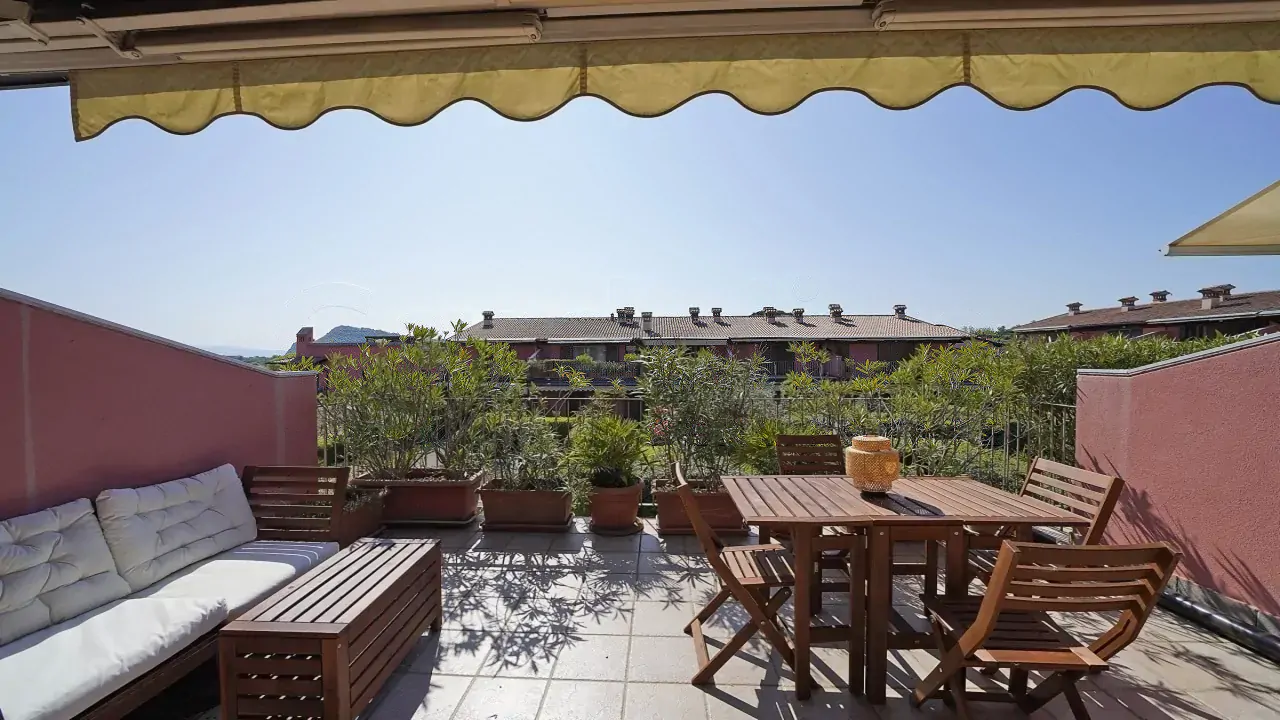 Terrasse mit Holztisch und Stühlen und Sofa mit weißen Kissen