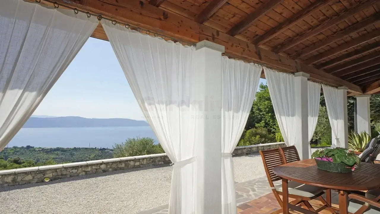 Überdachte Terrasse mit weißen Vorhängen und Blick auf den Gardasee