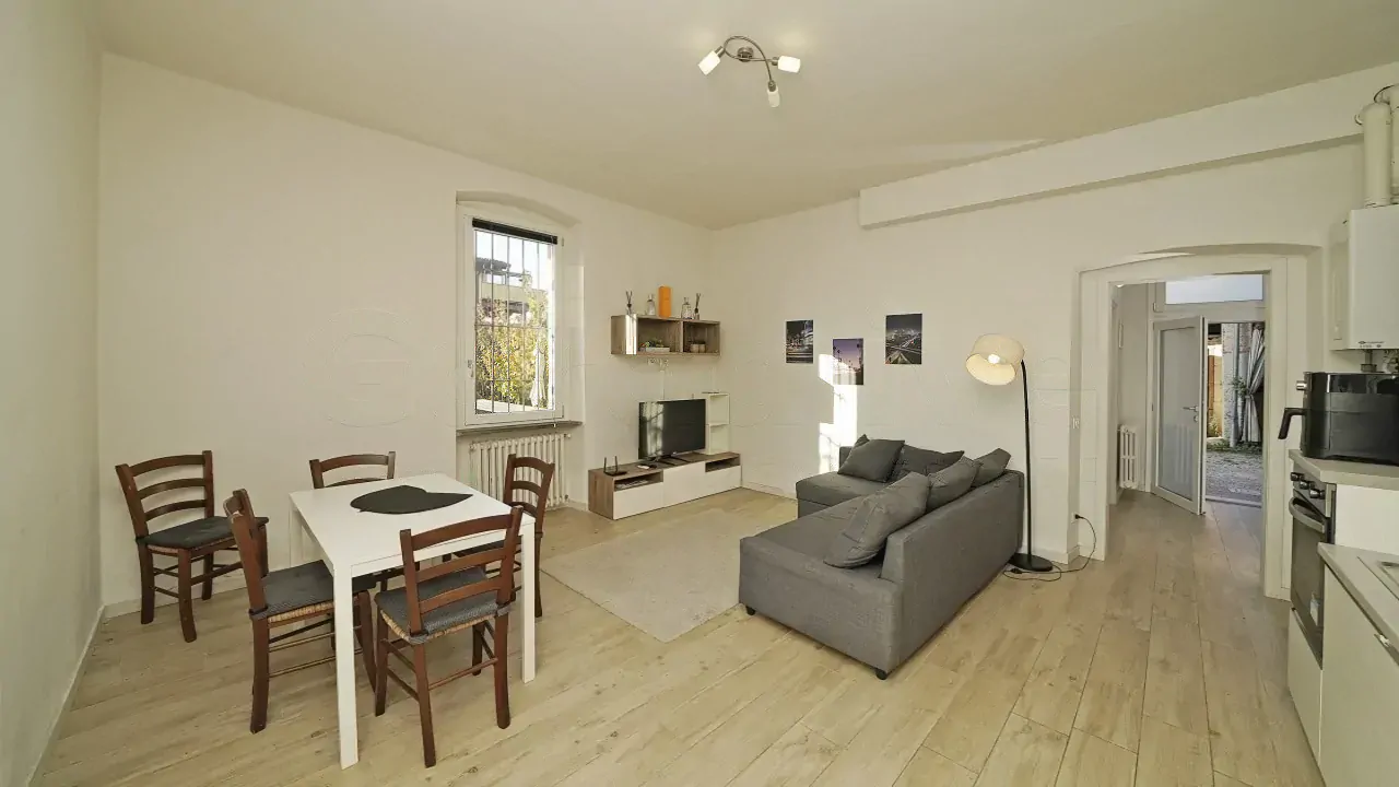 Wohnzimmer mit grauem Sofa, Esstisch und Fenster mit Gitter