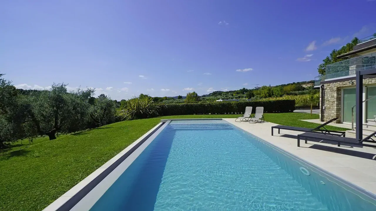 Piscina rettangolare con prato e sedie a sdraio