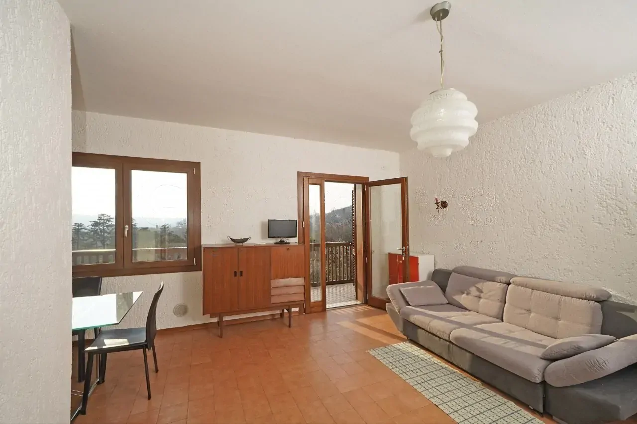 Soggiorno con divano grigio e porta finestra aperta sul balcone