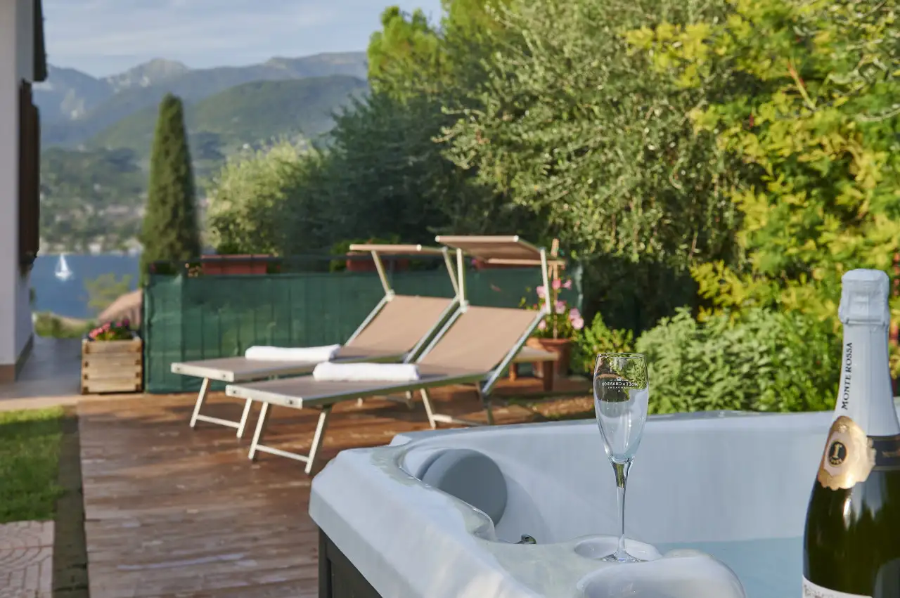 Whirlpool mit Glas und Flasche auf Terrasse mit Liegestühlen und Grün