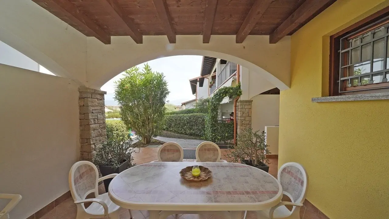 Portico con tavolo e sedie in plastica bianca e vista su giardino e vialetto