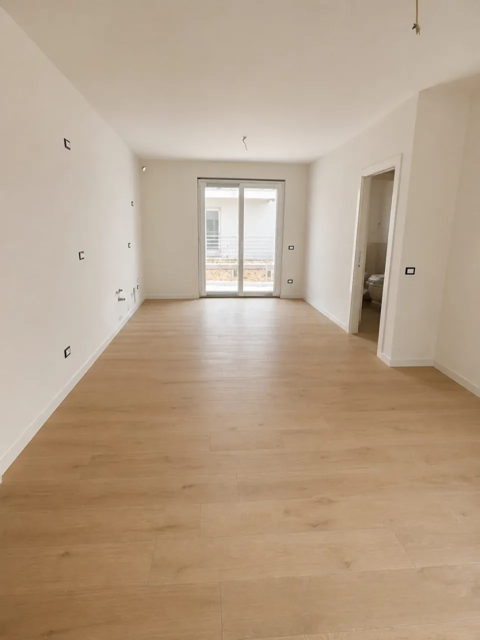 Soggiorno vuoto con pavimento in legno chiaro e porta finestra