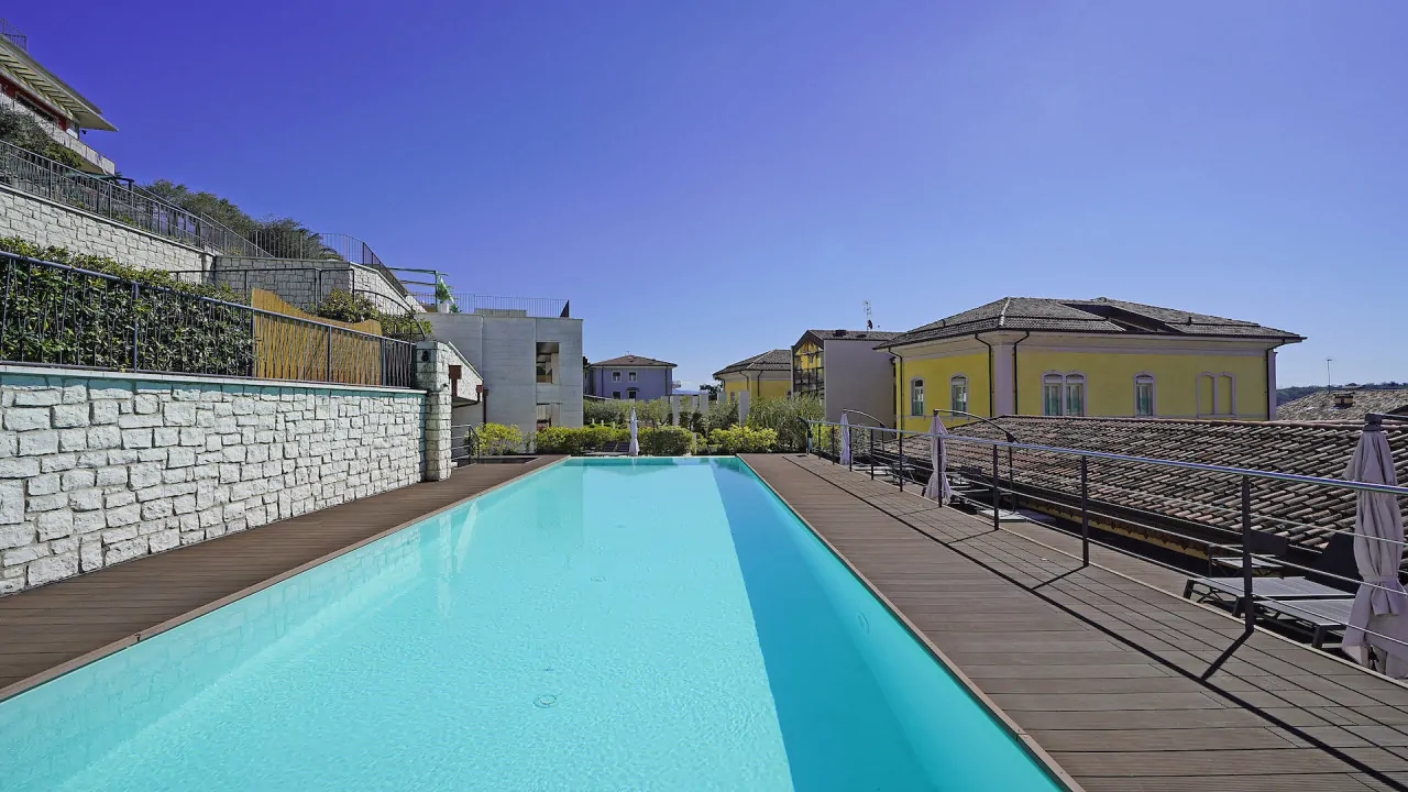 Swimming pool with wooden edge and stone wall under clear sky