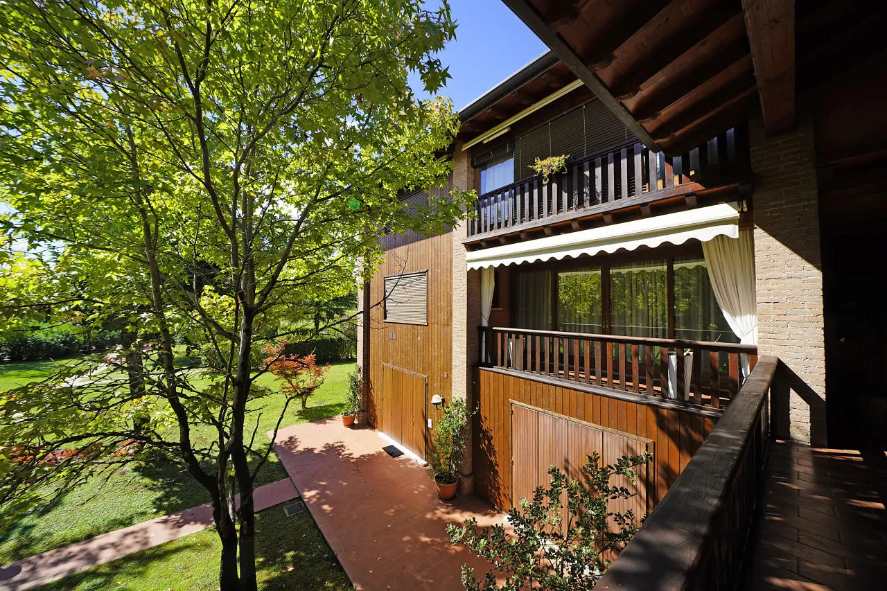 Facciata esterna con balcone e giardino verde con alberi