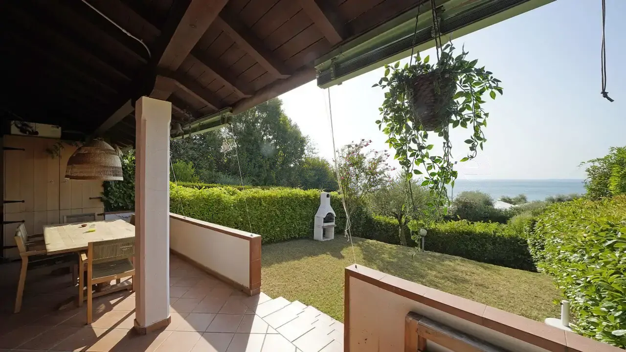 Covered terrace with table and view of garden and lake