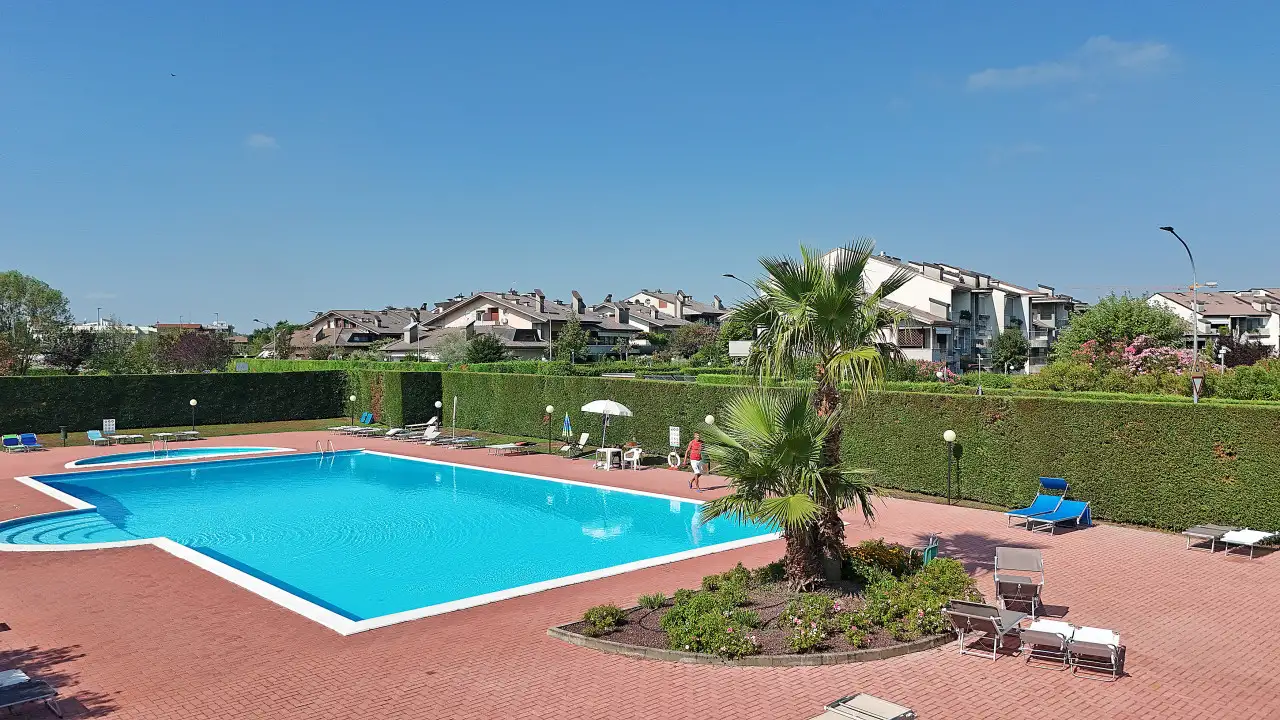 Piscina rettangolare con bordo bianco e area solarium con lettini e ombrelloni