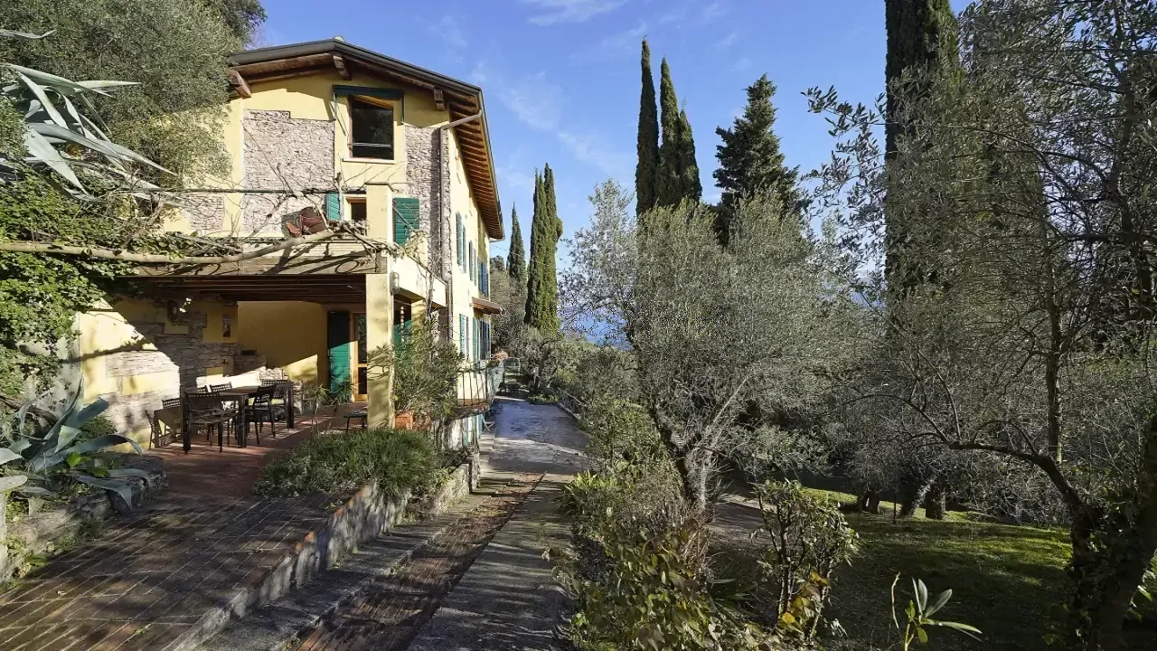 Facade of farmhouse with porch and garden with trees and cypresses