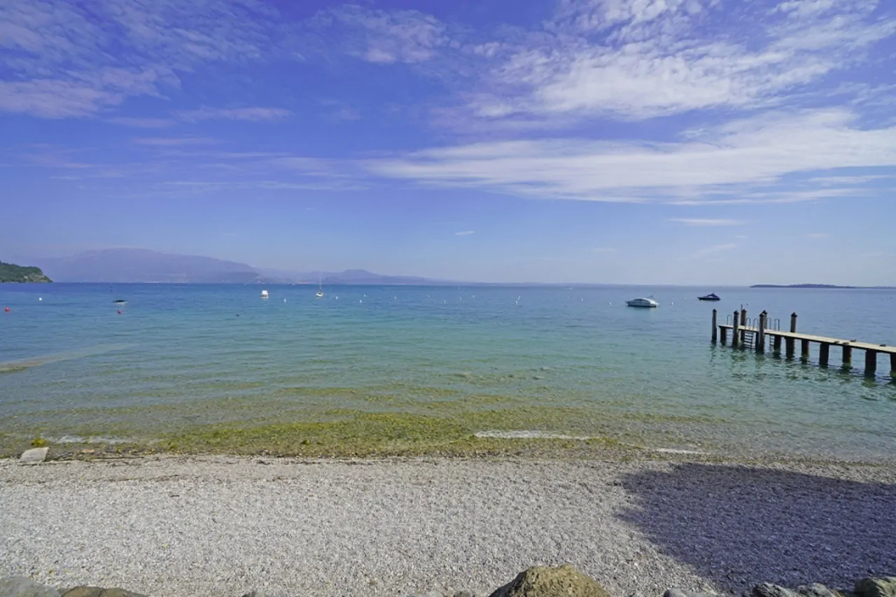 Spiaggia con acqua trasparente e pontile in legno sul lago a Manerba del Garda