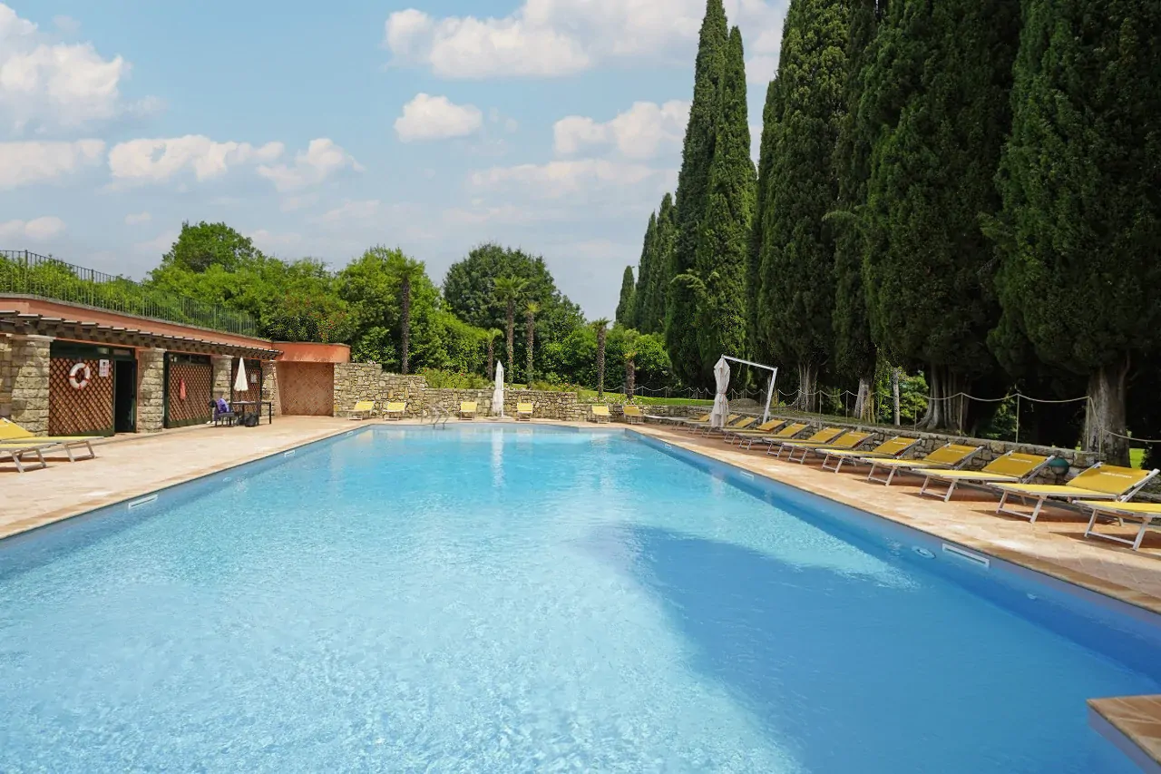 Schwimmbad mit Liegestühlen und hohen Bäumen auf der rechten Seite