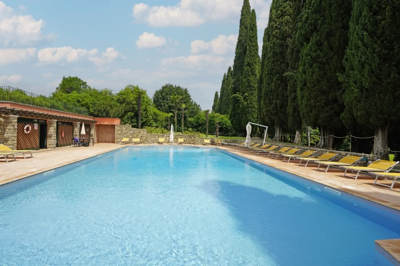 Schwimmbad mit Liegestühlen und hohen Bäumen auf der rechten Seite