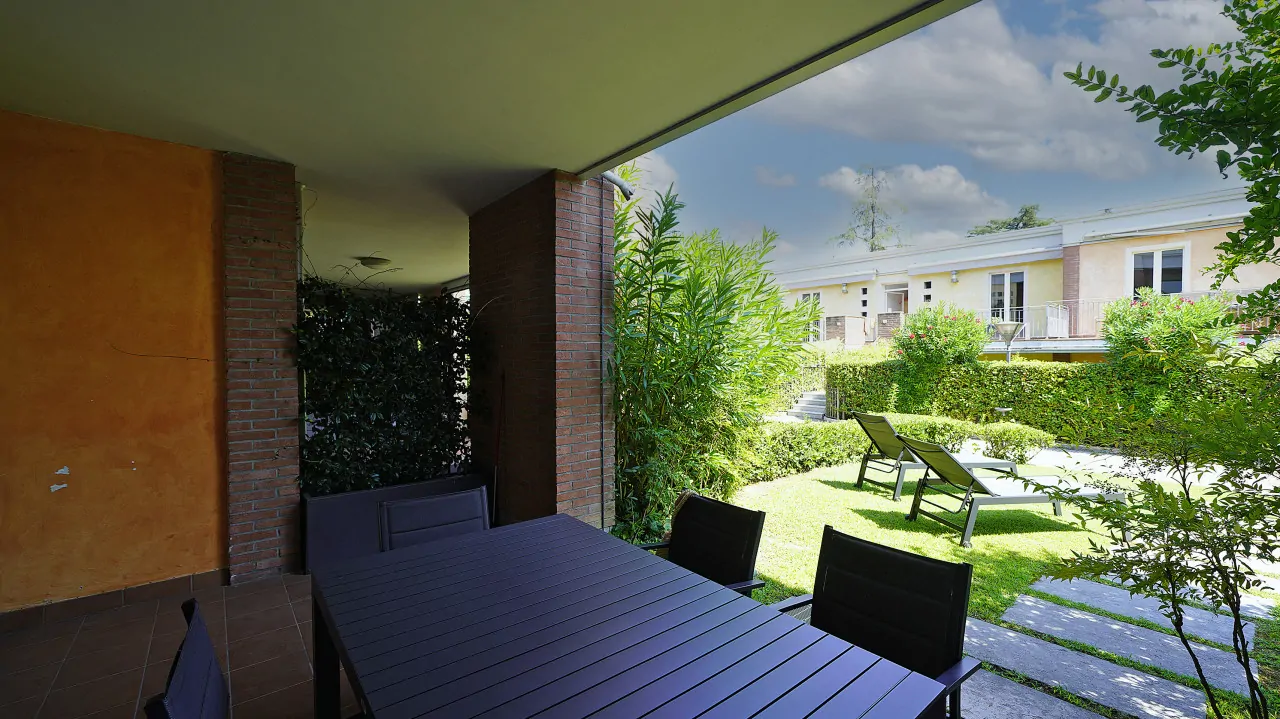 Portico con tavolo e sedie e vista sul giardino attrezzato con lettini