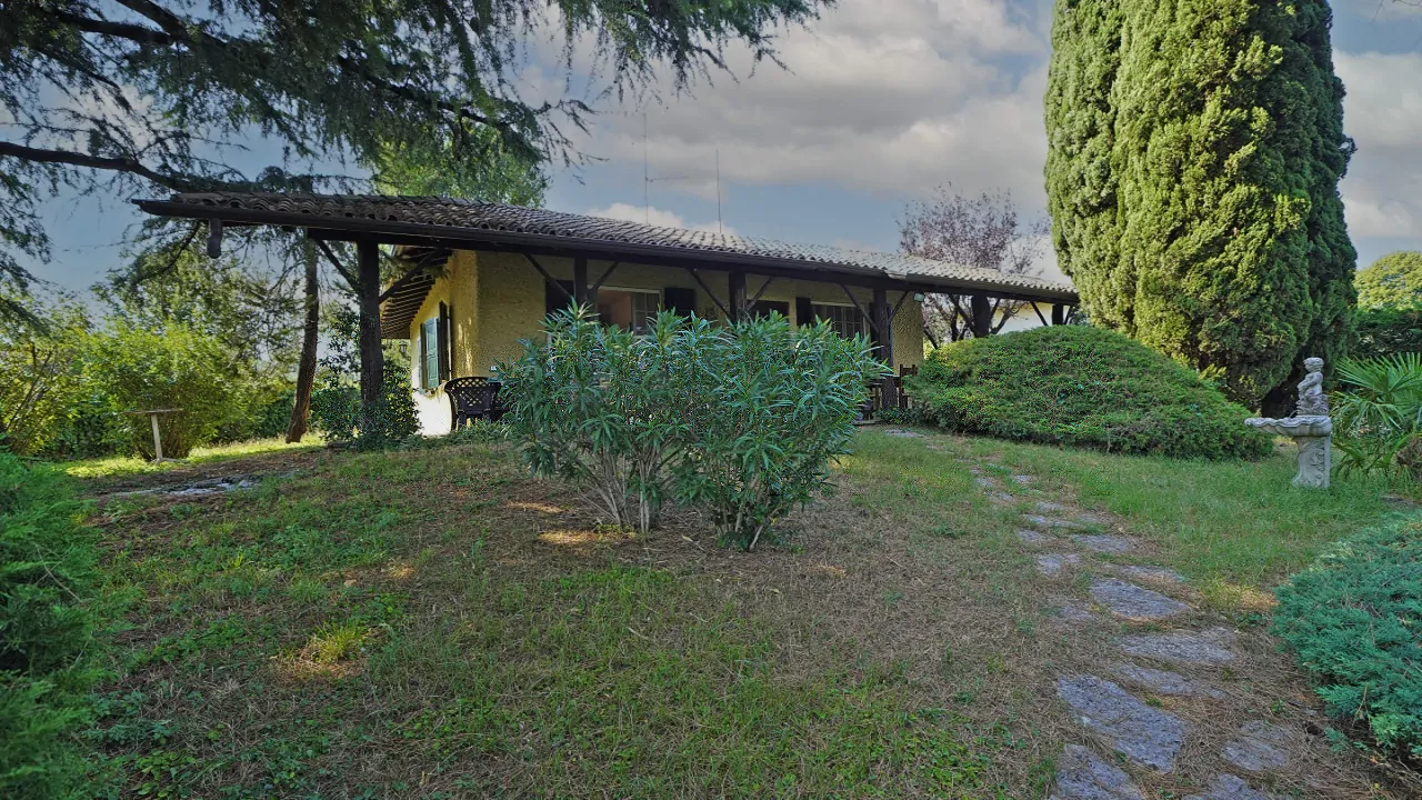 Giardino con prato, cespugli e vialetto in pietra davanti a villa con portico