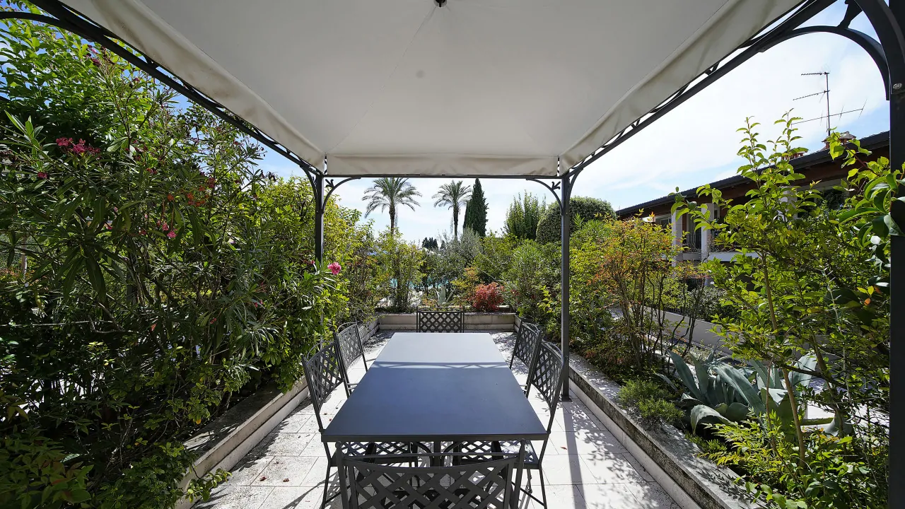 Pavillon mit Tisch und Stühlen im Garten mit Pflanzen und Pool im Hintergrund